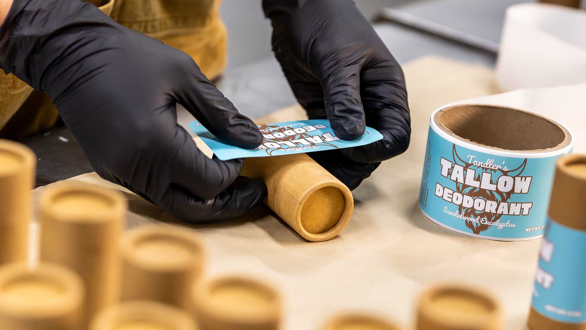 Person packaging Tallow Deodorant into cardboard tubes on a table.